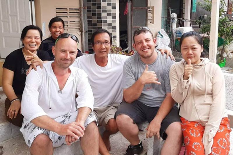 group photo of the Vietnam Seaweed Farmer and his family with Matthew Carpenter sitting on the back step of the porch at their home during a sunny day