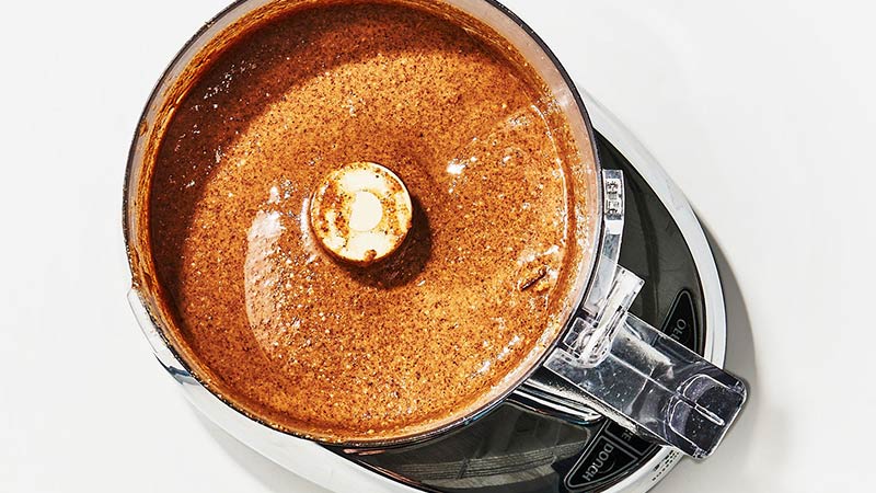 What is Nut Butter? A Natural Plant Based Alternative. Image of a food processor with hazelnut butter being made. This is a rich coffee brown colour with a slick glazed appearance to it in a modern looking food processor