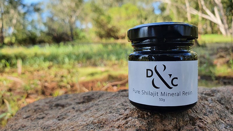 Shilajit Resin-Nature's Mineral Dense High Altitude Extract Featured Image with a photograph of a jar of Shilajit sitting on rock in Kakadu National Park with a lush green creek behind it
