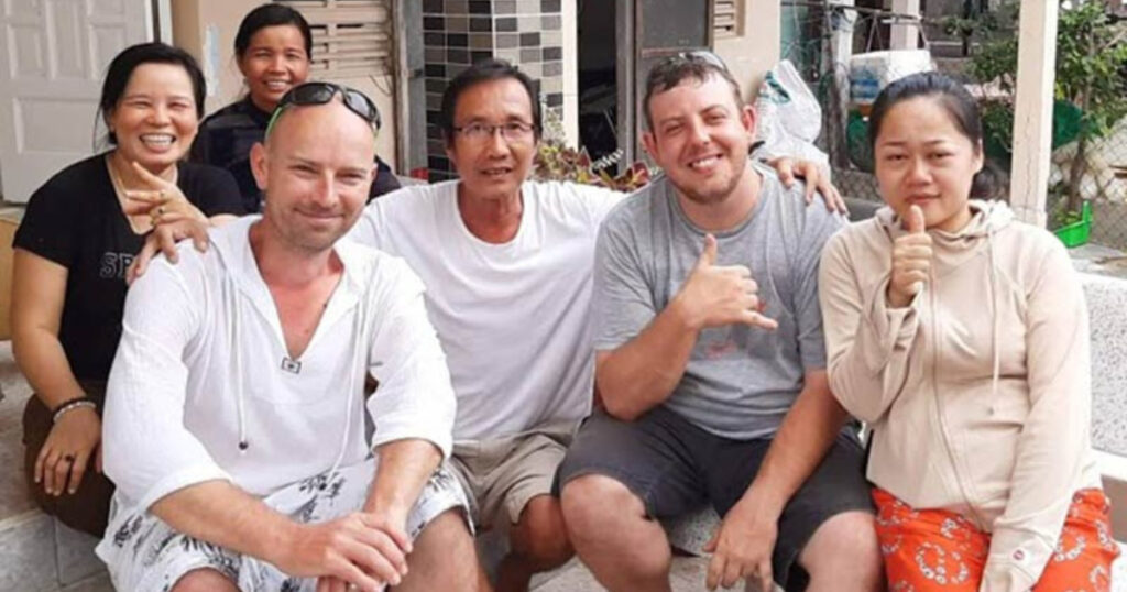 group photo of the Vietnam Seaweed Farmer and his family with Matthew Carpenter sitting on the back step of the porch at their home during a sunny day